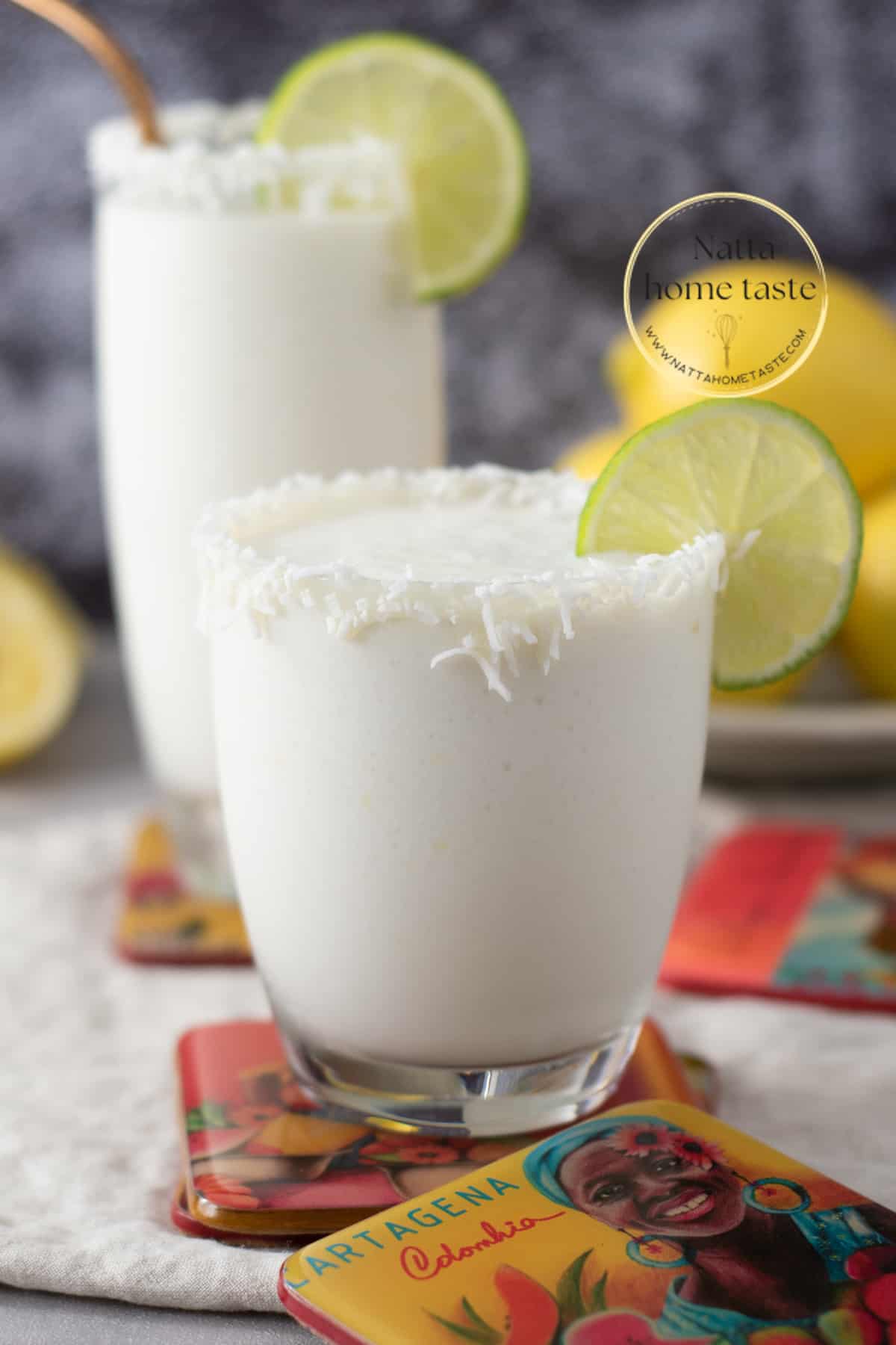 Toma frontal de dos vasos de cristal con limonada de coco servidos con rodajas de limón sobre porta vasos de Cartagena de Indias. 