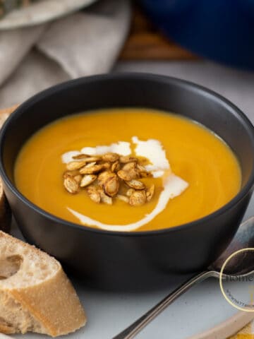 Sopa de calabaza servida en un bol negro con semillas de calabaza tostadas y pan crujiente