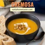 Sopa de calabaza servida en un bol negro con semillas de calabaza tostadas y pan crujiente