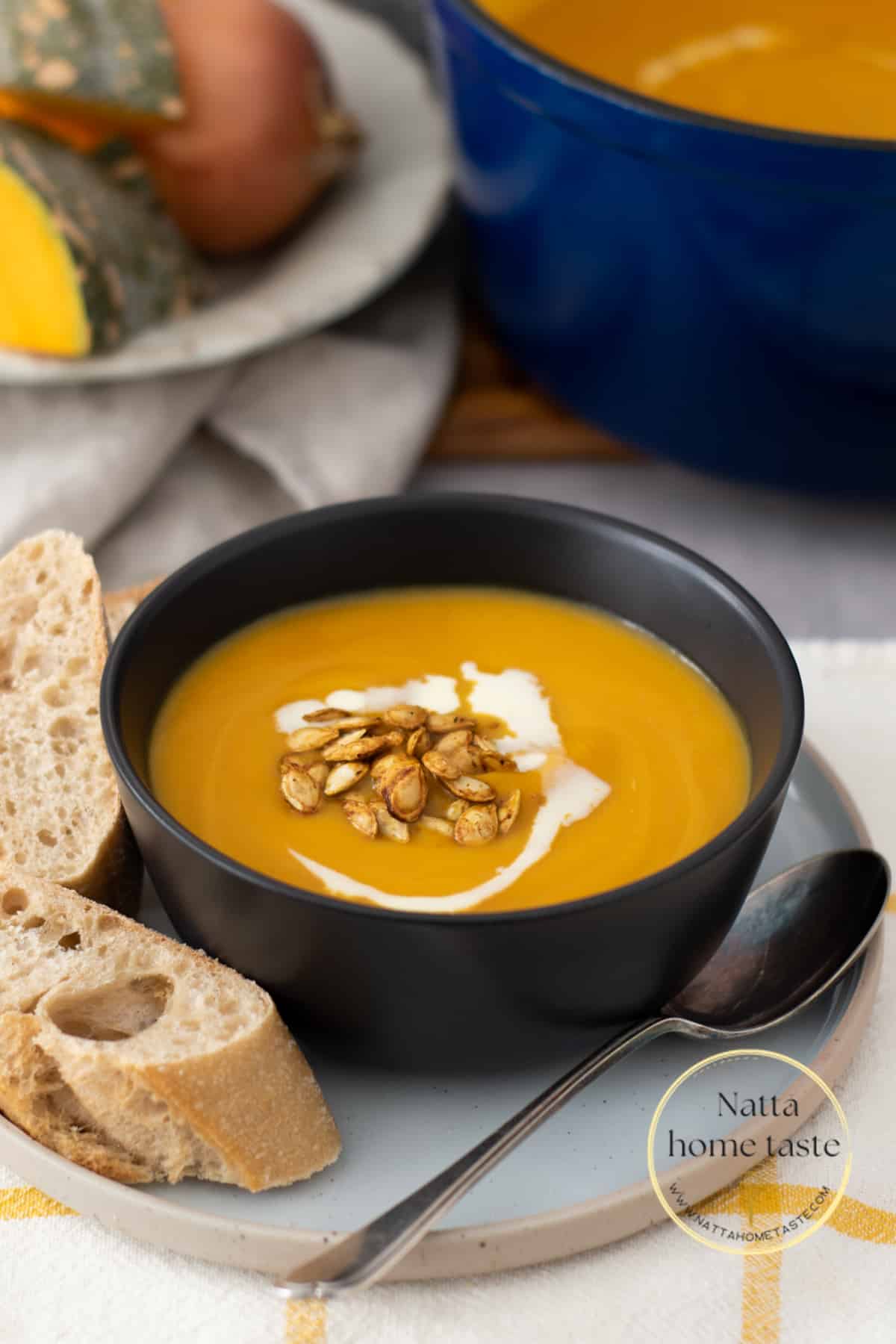 Sopa de calabaza servida en un bol negro con semillas de calabaza tostadas y pan crujiente
