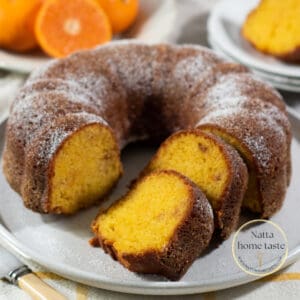 Torta de mandarina redonda servida en un plato blanco con mandarinas frescas en la parte de atrás.