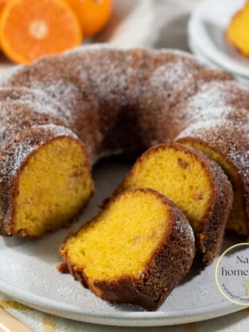 Torta de mandarina redonda servida en un plato blanco con mandarinas frescas en la parte de atrás.