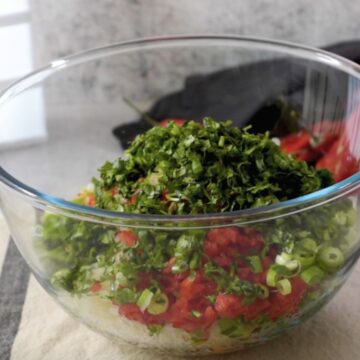 Tazón transparente con una mezcla de cebollas, pimentones rojo y verde, cilantro finamente picados 