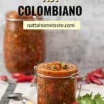 frasco de vidrio con ají picante colombiano sobre una mesa con una pequeña cuchara al lado y un manojo de cilantro fresco.