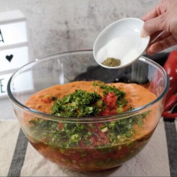 Tazón transparente con una mezcla de cebollas, pimentones, cilantro y ajíes licuados. y un pequeño plato con sal, pimienta y azúcar. 