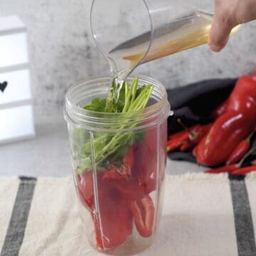 Vaso plástico de licuadora con ajíes, cilantro y vinagre de manzana.