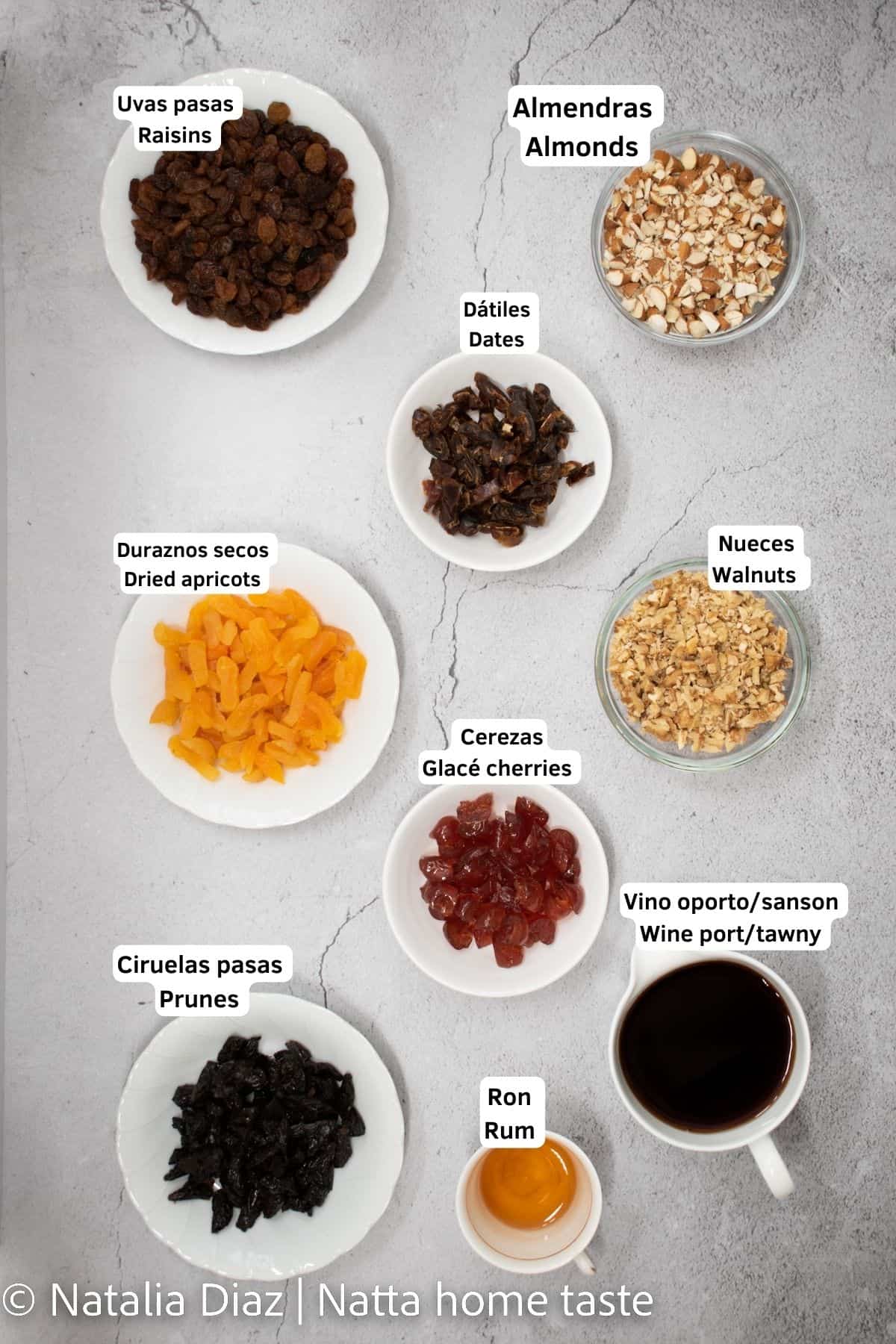 ingredientes para macerado de frutas secan para torta envinada. todos los ingredientes están en pequeños contenedores redondos. uvas pasas, almendras, dátiles, duraznos secos, nueces, cerezas, ciruelas pasas, ron y vino oporto.