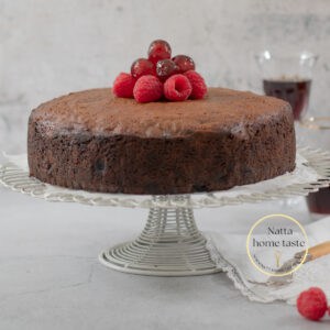 Torta Negra sobre una base para pasteles de alambre blanco con cerezas en la parte de arriba y una copa de vino en la parte de atrás.