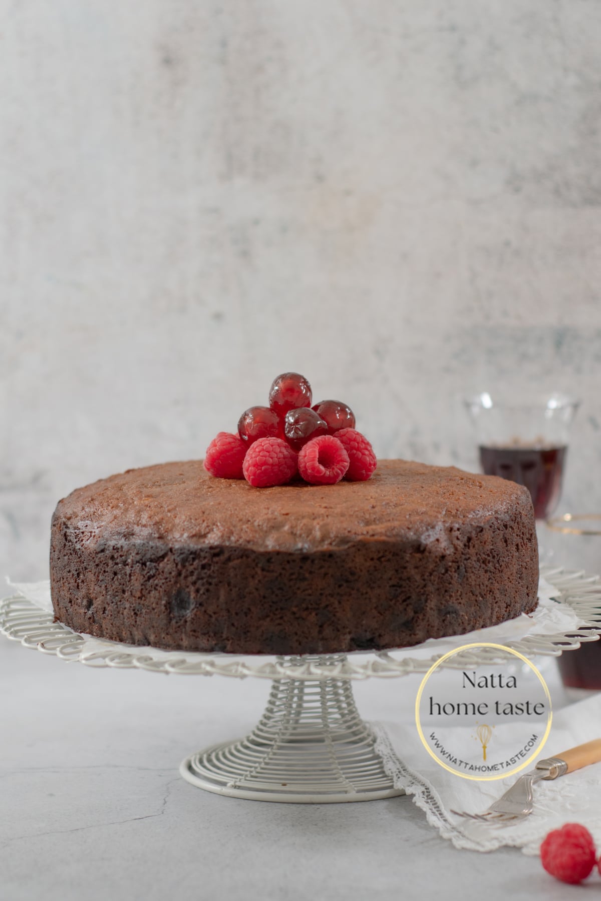 Torta Negra sobre una base para pasteles de alambre blanco con cerezas en la parte de arriba y una copa de vino en la parte de atrás.