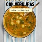 imagen desde arriba de una olla blanca con sopa de pasta con verduras y una cuchara de madera.