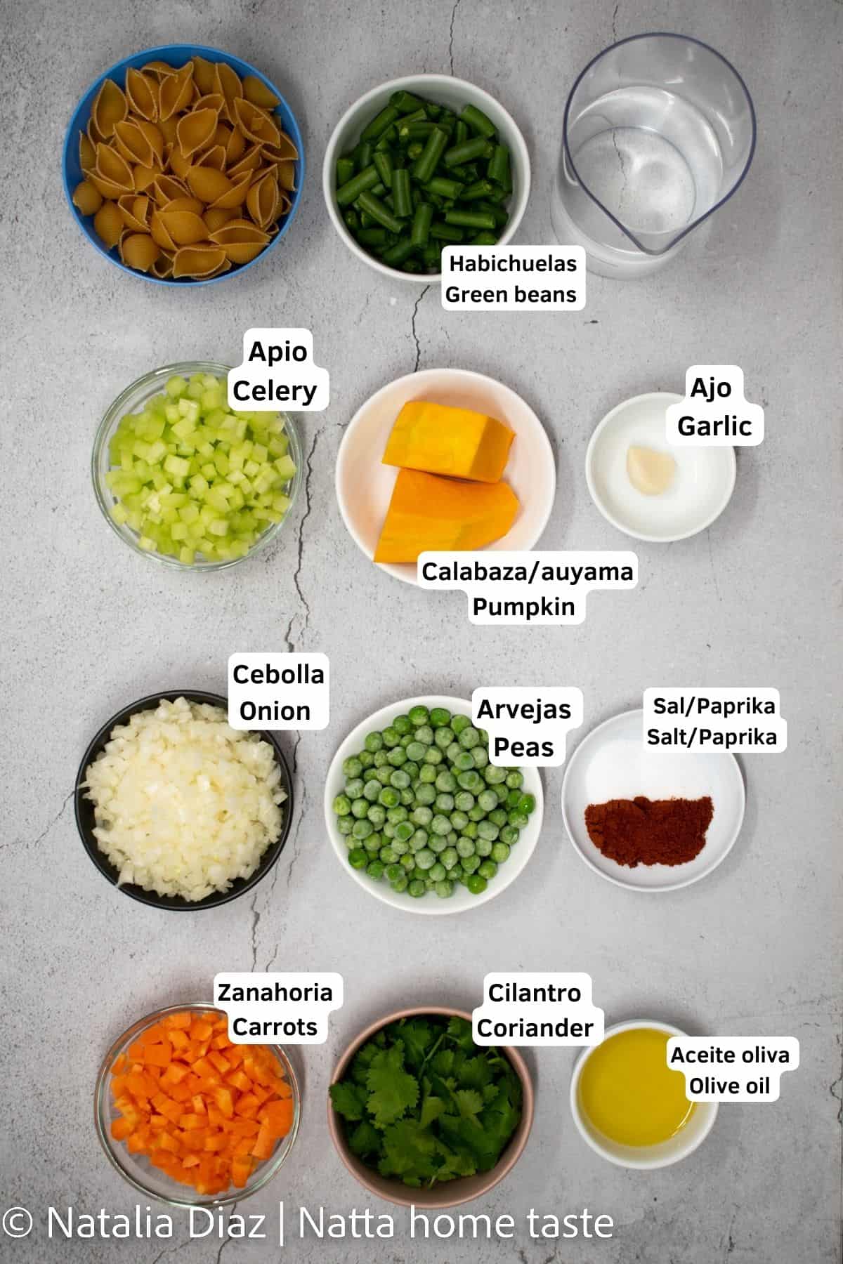 ingredientes para preparar sopa de pasta con verduras. Todos los ingredientes están en pequeños contenedores redondos. Pasta en conchitas, habichuelas, agua, apio, auyama, ajo, cebolla, arvejas, sal, paprika, zanahoria, cilantro, aceite de oliva.