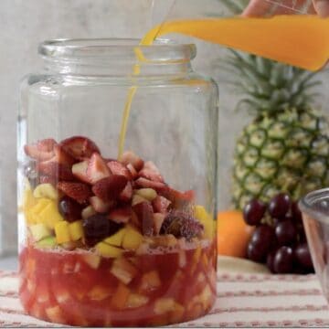 contenedor de vidrio grade con frutas tropicales en trozos con jugo de sandia y jugo de naranja.