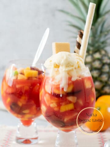 dos copas de salpicón de frutas colombino con helado de vainilla y galletas wafer con una piña entera y los mandarinas en la parte de atrás.