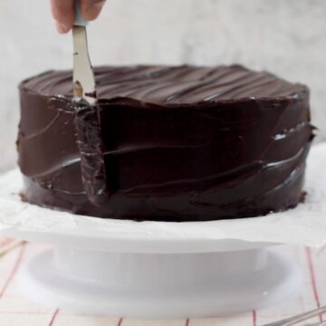 torta de chocolate siendo cubierta con ganache de chocolate con una espátula sobre una base giratoria.