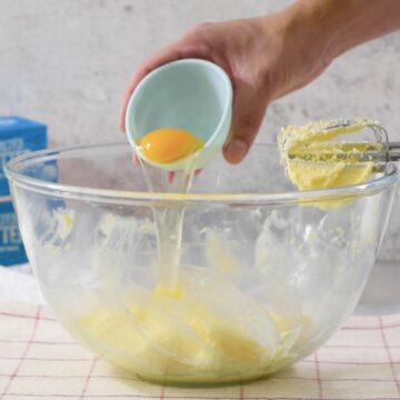 Tazón transparente con una mezcla de mantequilla y un huevo con una batidora de mano.