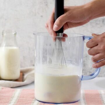 mezcla de leche, crema de leche y huevos en una jarra transparente con un batidor de mano.