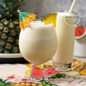 dos vasos con piña colada, un vaso con una sombrilla de coctel y el otro con un pitillo de madera. Una piña entera en la parte de atrás.