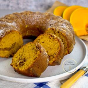 budín de calabaza redondo sobre un plato blanco con rodajas de calabaza fresca en la parte de atrás