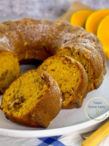 budín de calabaza redondo sobre un plato blanco con rodajas de calabaza fresca en la parte de atrás