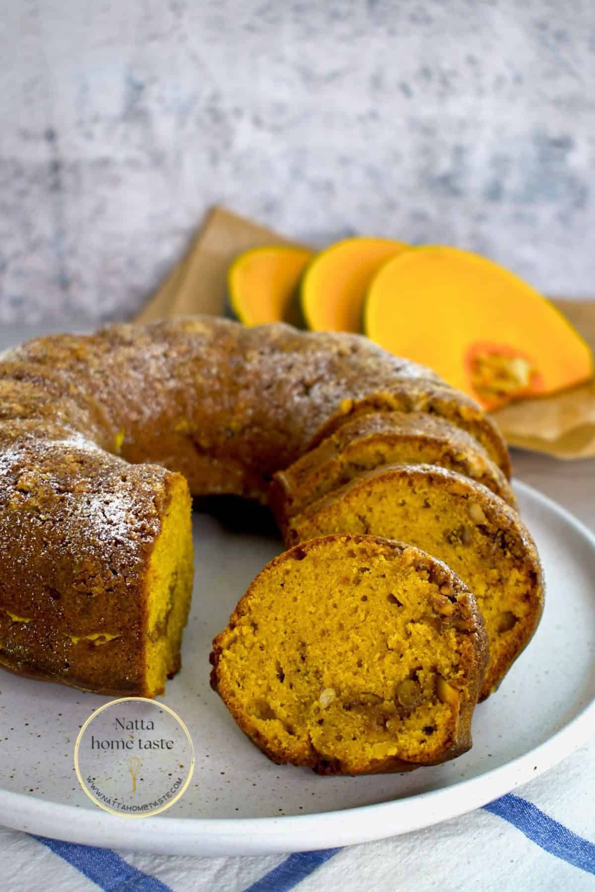 budín de calabaza redondo sobre un plato blanco con rodajas de calabaza fresca en la parte de atrás