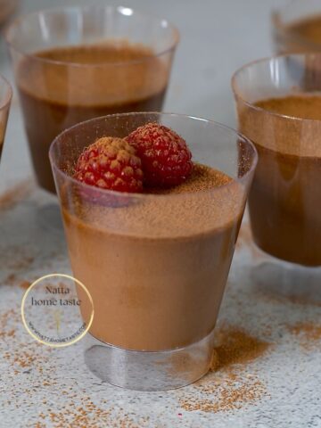 mousse de chocolate sin azúcar en vasitos transparente sobre una mesa gris con frambuesas encima