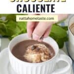 taza de chocolate caliente con crema batida y trozos de chocolate sobre un plato blanco redondo
