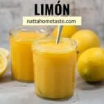 crema de limón servida en dos frascos de vidrio con una cuchara y varios limones amarillos alrededor.