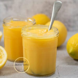 crema de limón servida en dos frascos de vidrio con una cuchara y varios limones amarillos alrededor.