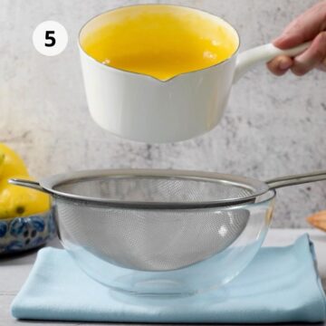 Tazón mediano con un colador y una olla pequeña con crema de limón caliente.