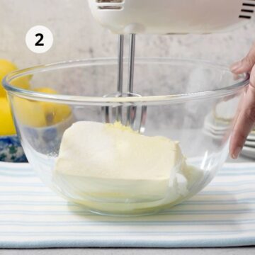 tazón grande de vidrio con queso crema y una batidora eléctrica de mano