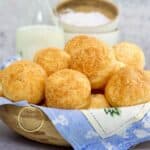 pan de queso brasileño en un tazón de madera con un litro de leche atrás y tazones pequeños de madera con harina de tapioca