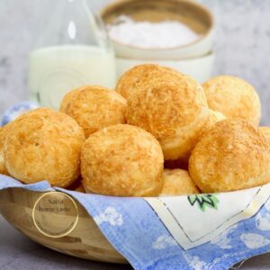 pan de queso brasileño en un tazón de madera con un litro de leche atrás y tazones pequeños de madera con harina de tapioca