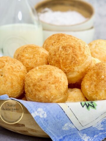 pan de queso brasileño en un tazón de madera con un litro de leche atrás y tazones pequeños de madera con harina de tapioca