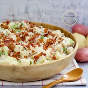 ensalada de papa en un contenedor de de madera sobre una mesa con una cuchara de madera al lado.