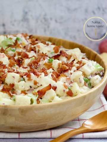 ensalada de papa en un contenedor de de madera sobre una mesa con una cuchara de madera al lado.
