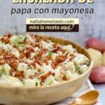 ensalada de papa en un contenedor de de madera sobre una mesa con una cuchara de madera al lado.