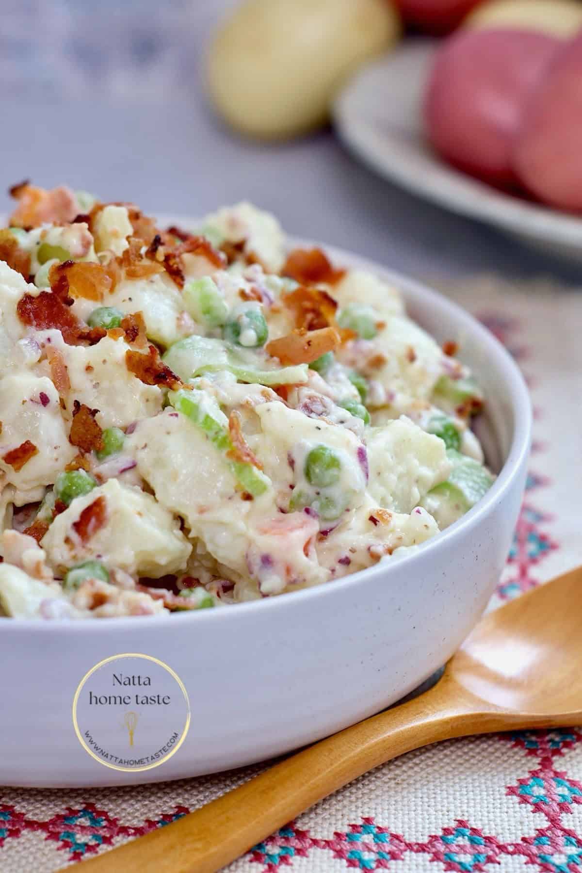 ensalada de papa en un contenedor blanco redondo sobre una mesa colorida y una cuchara de madera