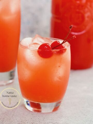 limonada cereza en un vaso de vidrio con hielo y dos cerezas en almíbar.