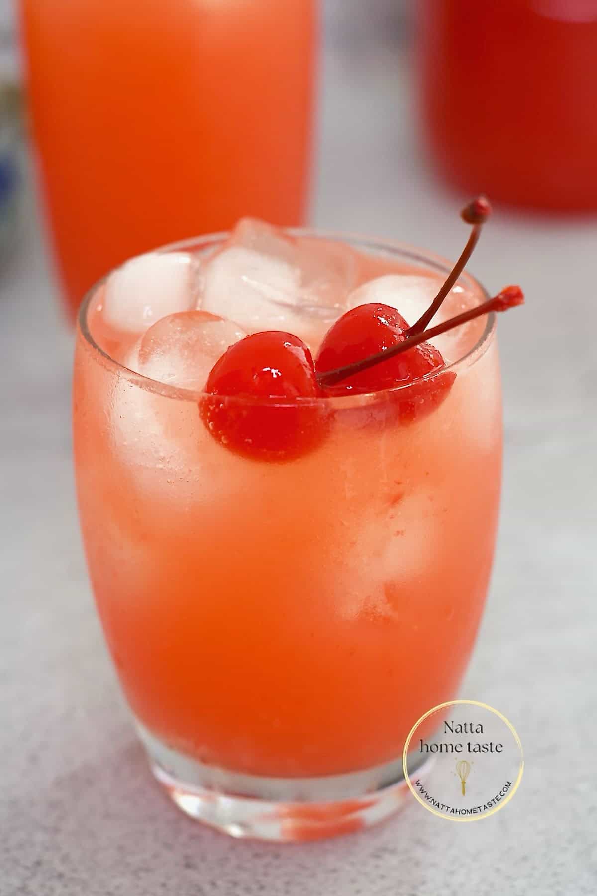 limonada cereza en un vaso de vidrio con hielo y dos cerezas en almíbar.