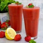 dos vasos de vidrio con mojito de fresa fresas y limón frescos al lado