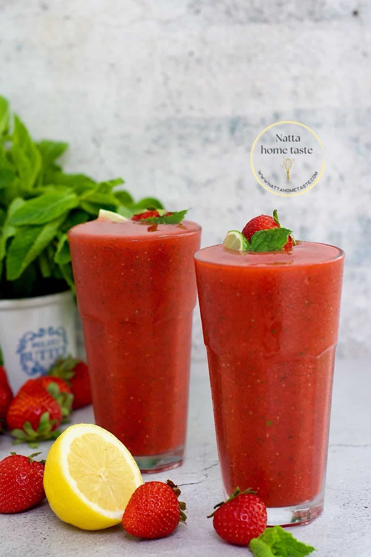 dos vasos de vidrio con mojito de fresa fresas y limón frescos al lado