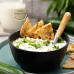 salsa griega de pepino y yogur en un contenedor negro sobre un plato redondo con una cuchara de madera