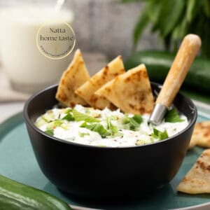 salsa griega de pepino y yogur en un contenedor negro sobre un plato redondo con una cuchara de madera