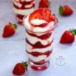 Dos vasos de fresas con crema en capas, decorados con fresas frescas y servidos en una mesa con fondo rosa. Un postre cremoso y delicioso, ideal para vender o disfrutar en casa.
