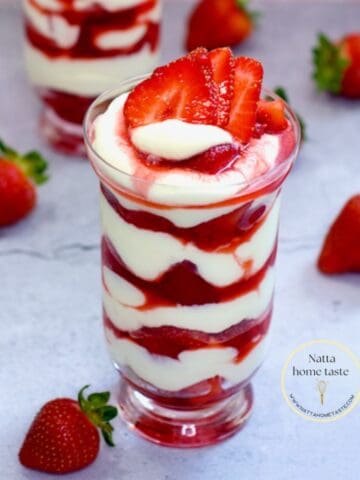 Dos vasos de fresas con crema en capas, decorados con fresas frescas y servidos en una mesa con fondo rosa. Un postre cremoso y delicioso, ideal para vender o disfrutar en casa.