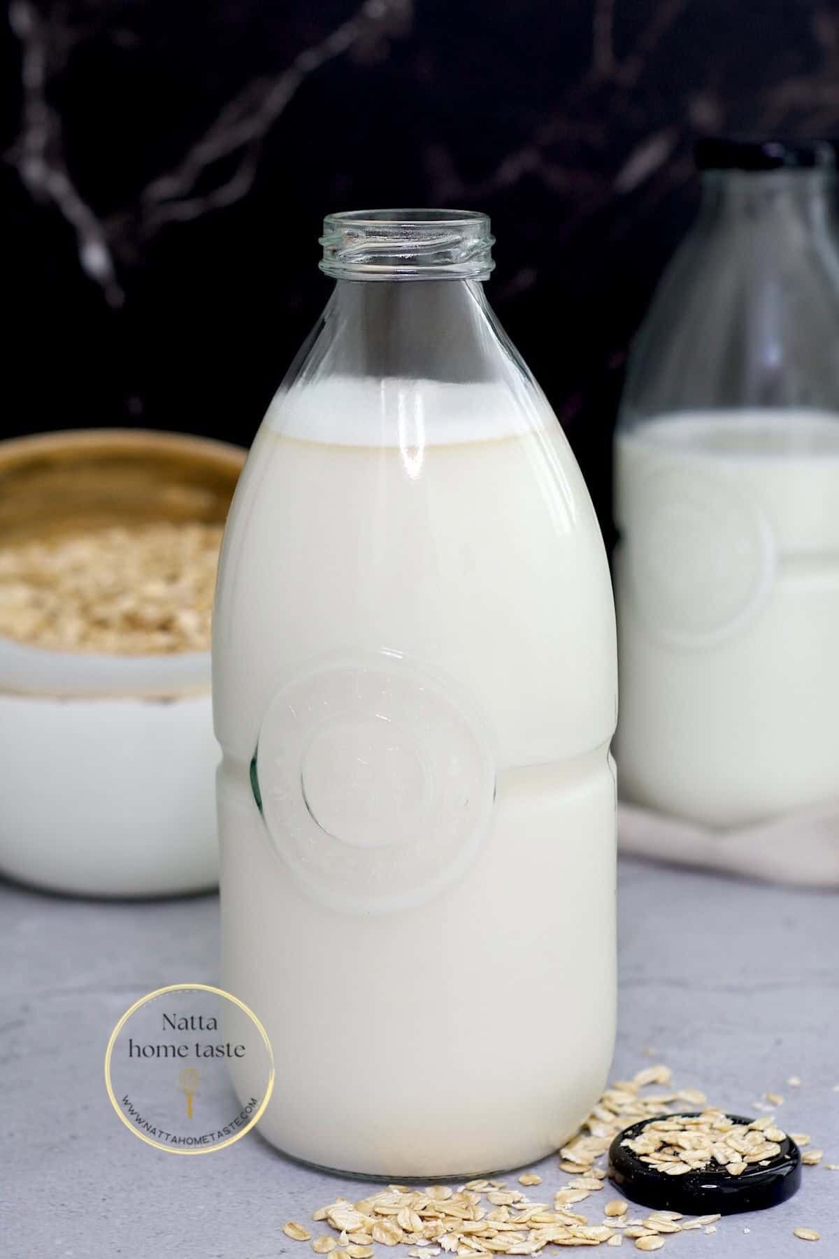leche de avena casera en un frasco de vidrio sobre una mesa con una taza de avena en copos en la parte de atrás.