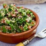 ensalada tabulé servida en un contenedor redondo de color café sobre una mesa con un tenedor al lado.