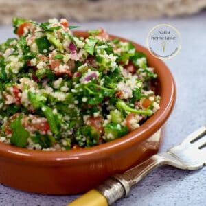 ensalada tabulé servida en un contenedor redondo de color café sobre una mesa con un tenedor al lado.