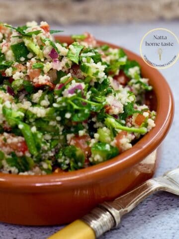ensalada tabulé servida en un contenedor redondo de color café sobre una mesa con un tenedor al lado.