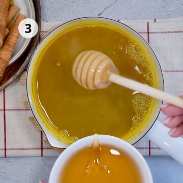 Agregando miel a infusión caliente en un tazón, con una cuchara de madera de miel suspendida sobre el líquido amarillo brillante.